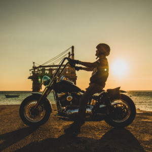 man resting on his motorcycle against the backdrop of a sun setting on the ocean