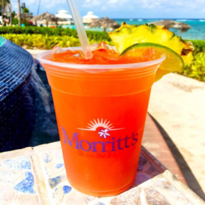 Bright red glass of rum punch, garnished with wedges of pineapple and lime