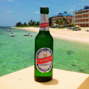 A Cayman Islands Caybrew beer sitting against a backdrop of the blue Caribbean Sea