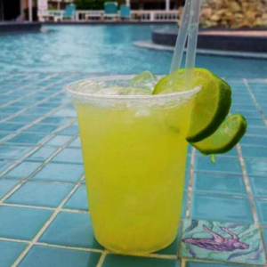 A bright green cocktail garnished with a slice of lime, placed by a poolside