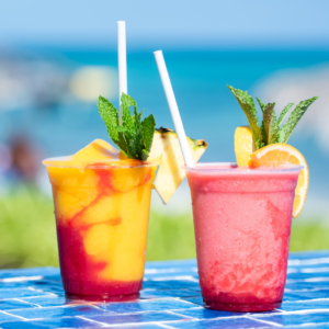 Two colourful cocktails garnished with lemon slices and mint sitting on an ocean backdrop