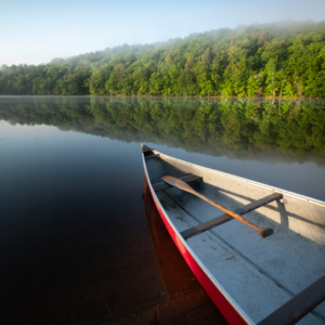 A close up view of the front of a red canoe in the middle of a serene lake, surrounded by a lush green forest